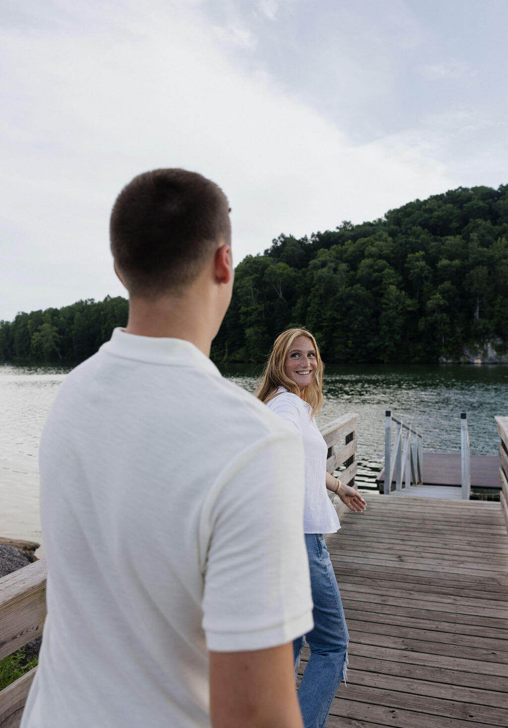 Woman smiling at her fiancé while standing together on a lakeside dock.