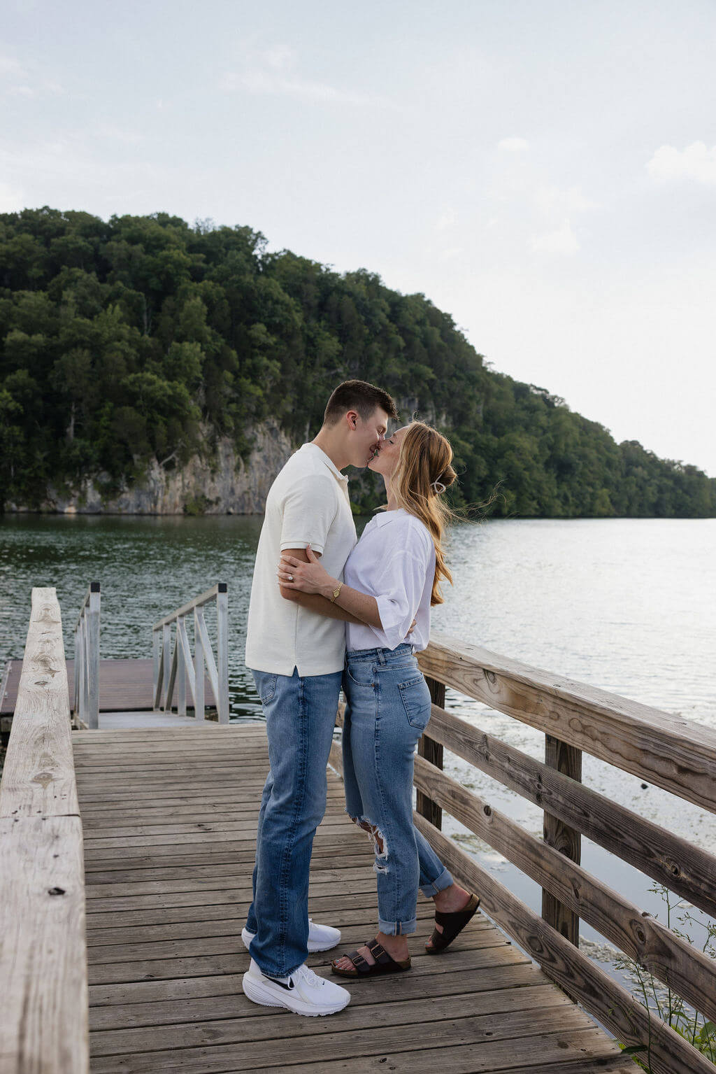 Engaged couple embracing on a wooden dock overlooking the lake.