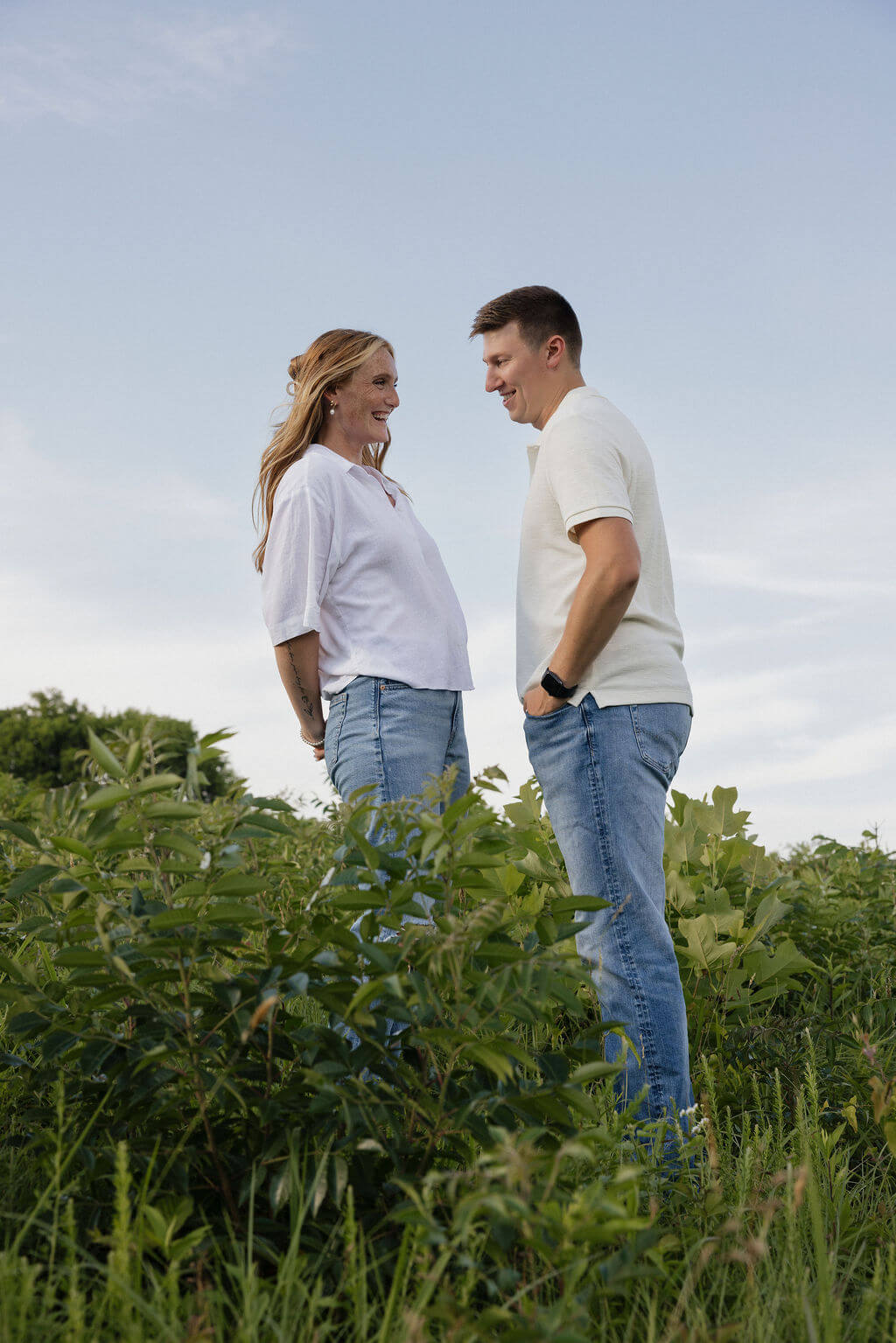 Couple smiling at each other while standing among tall green plants during their Knoxville engagement session.