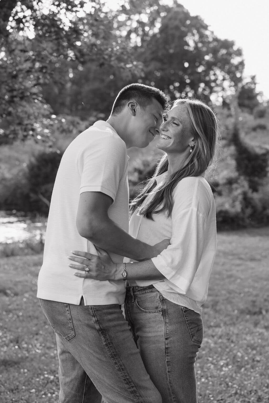 Black-and-white candid photo of an engaged couple laughing and dancing in a field.