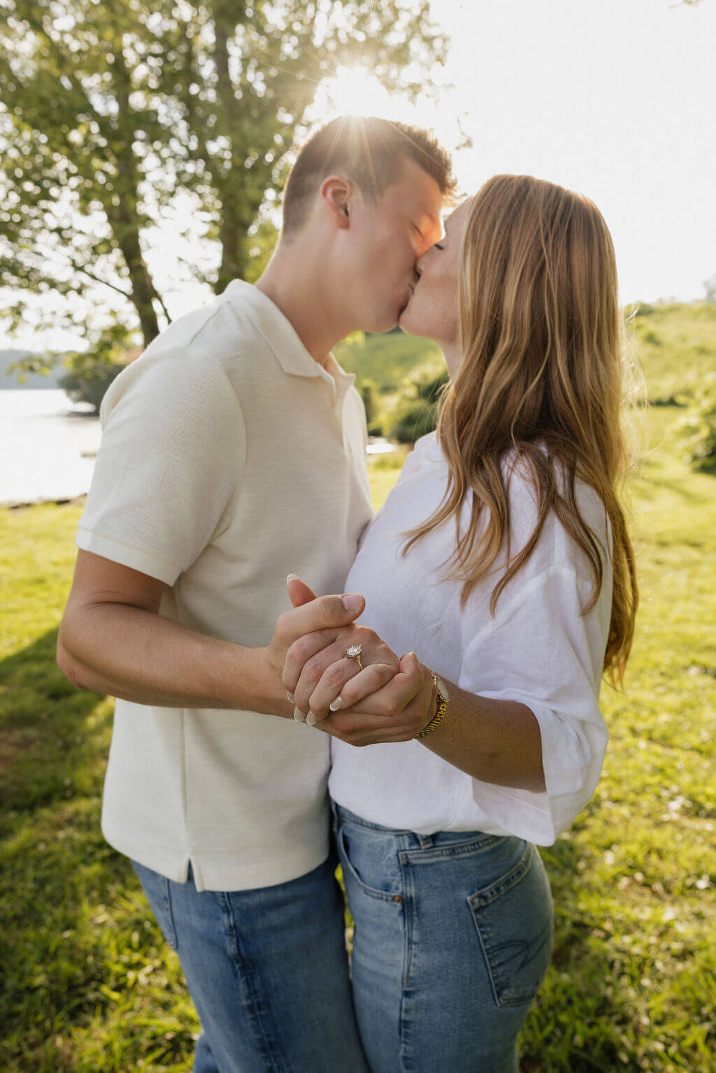 Couple kissing in warm evening light while holding hands during their engagement session.