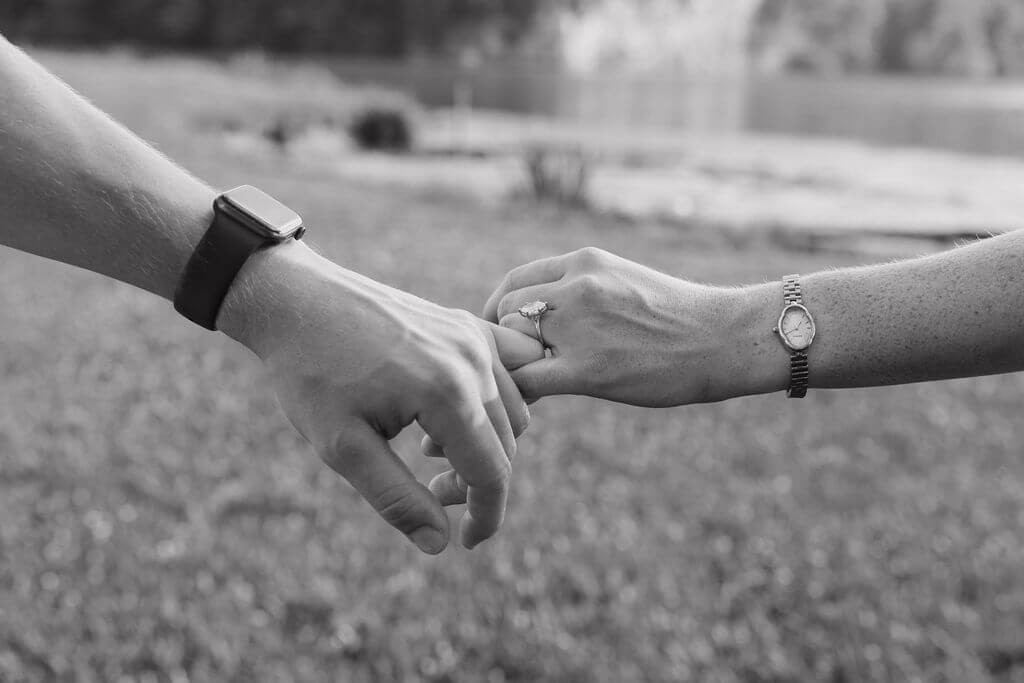 Black-and-white close-up of an engaged couple holding hands and showing the engagement ring.