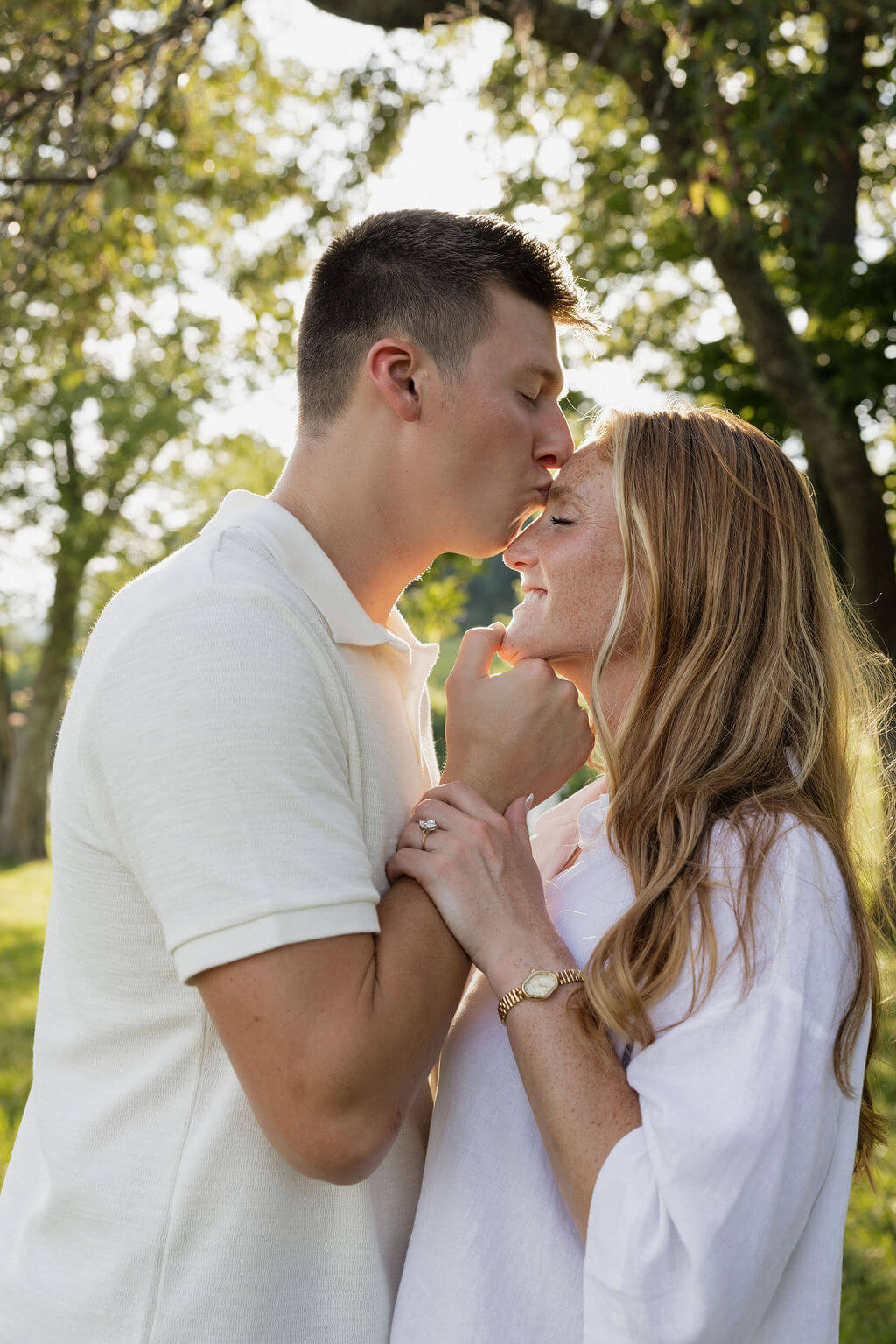 Couple sharing a quiet moment beneath a tree with warm sunlight glowing behind them.