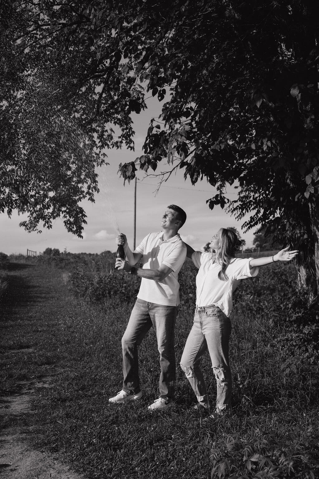 Black-and-white candid photo of a couple playfully dancing beneath a tree.