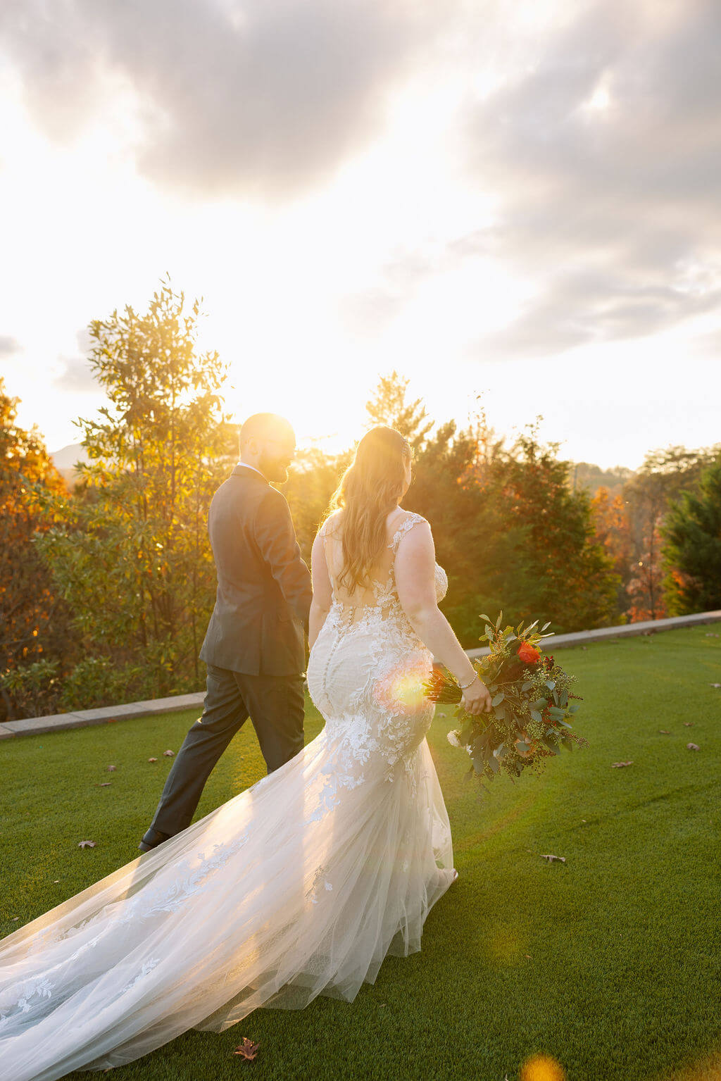 Newlyweds walk through golden sunset light on the lawn of a scenic fall wedding venue.