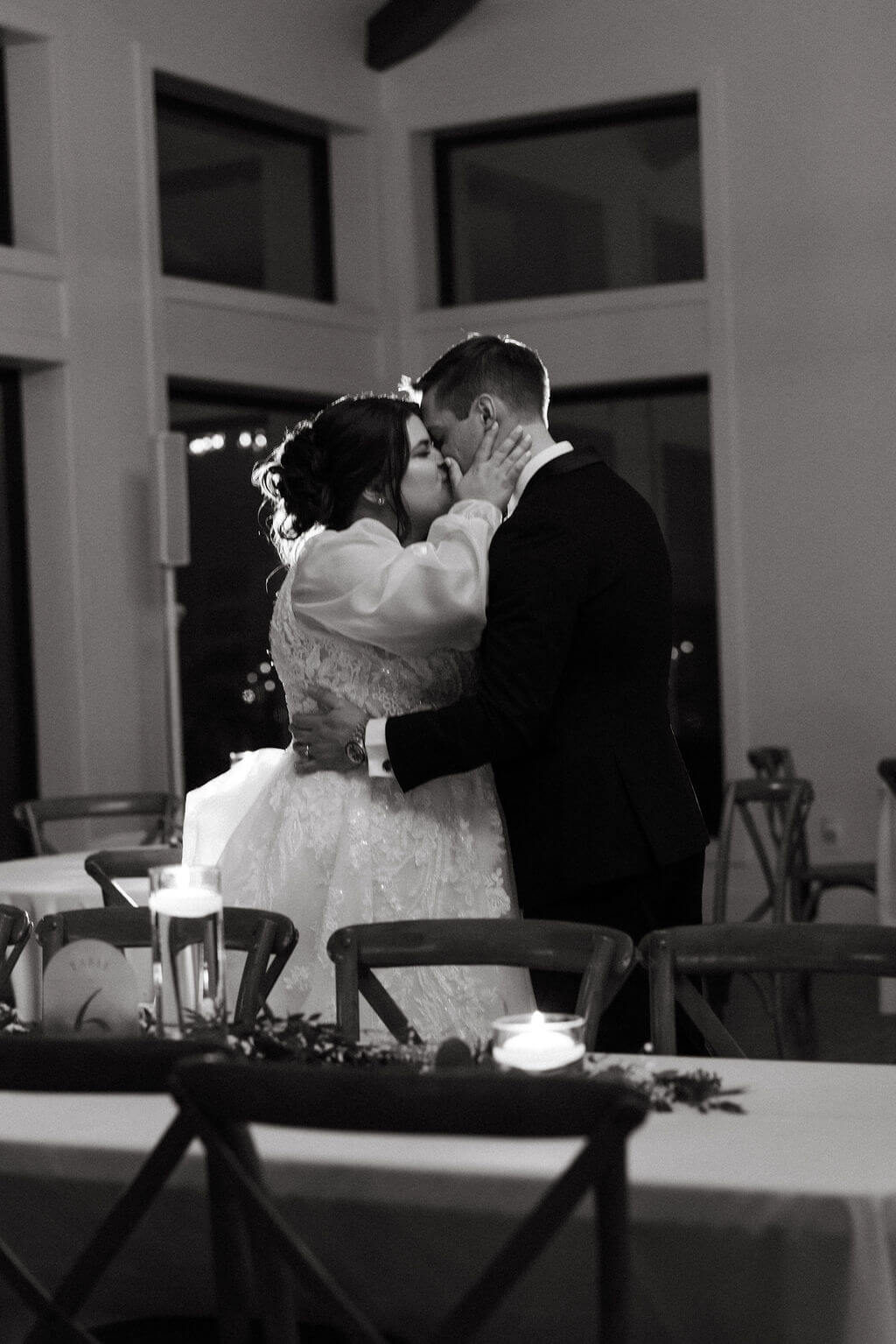 Black-and-white photo of newlyweds kissing during their indoor wedding reception.