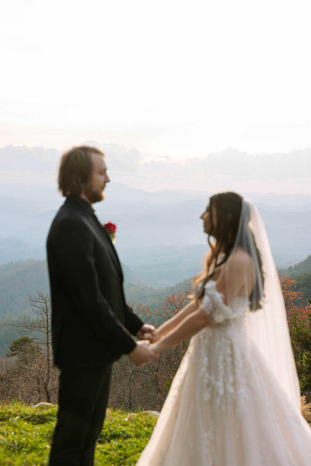 Couple holds hands during a softly focused portrait with layered mountain views behind them.