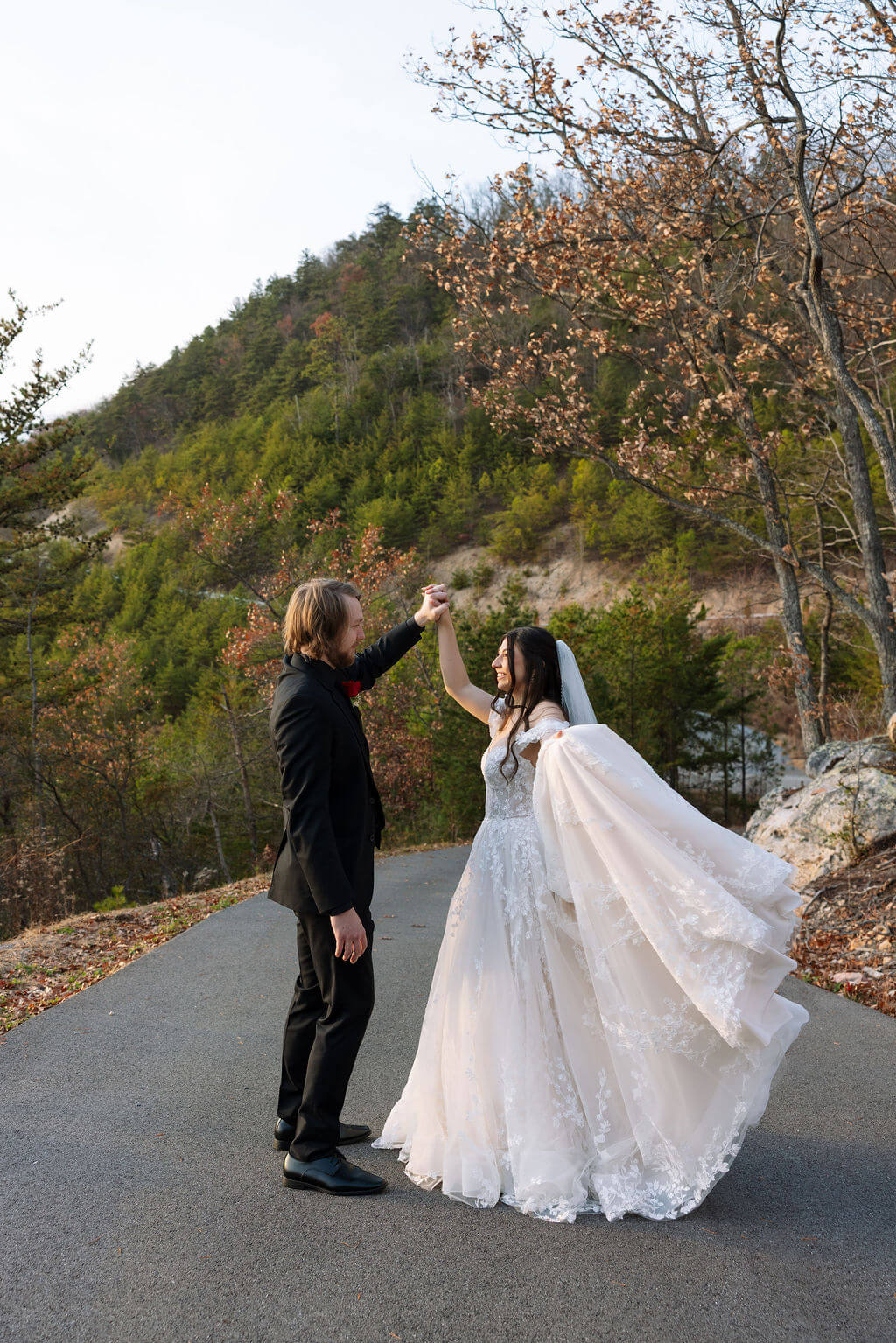 Partner twirls the bride on a mountain road as her wedding dress flows through the air.