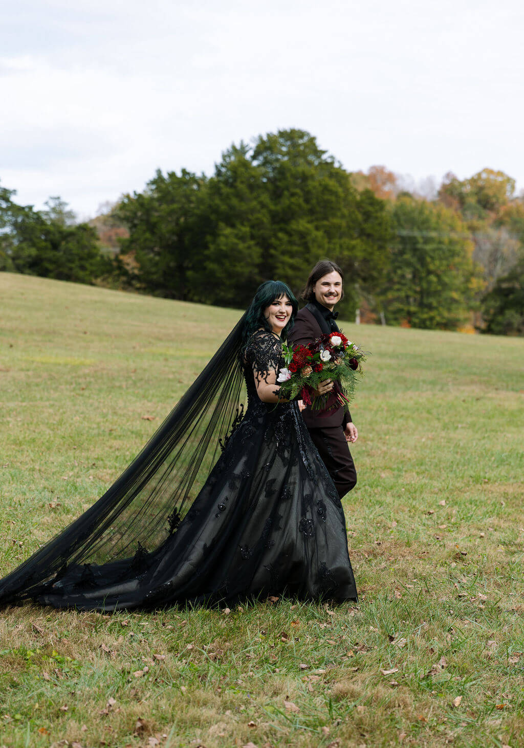 The couple walks through a field at Cove Lake State Park with the bride’s long black veil flowing behind them.