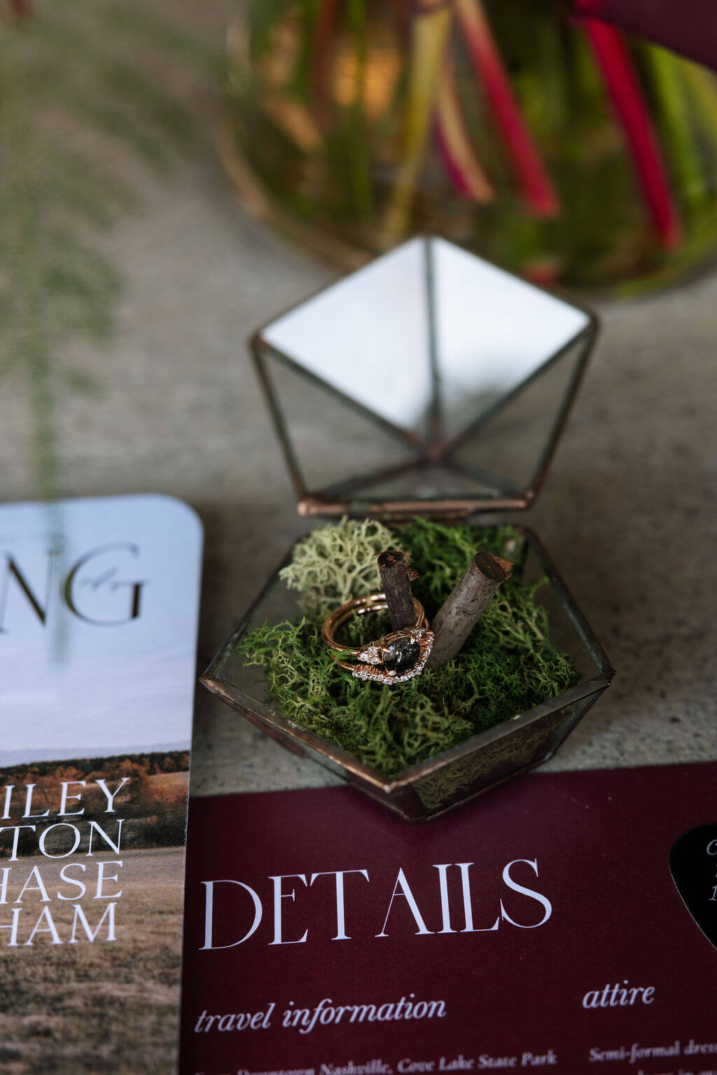 Burgundy wedding stationery, wedding rings in a glass box, and mossy details arranged for a fall wedding.