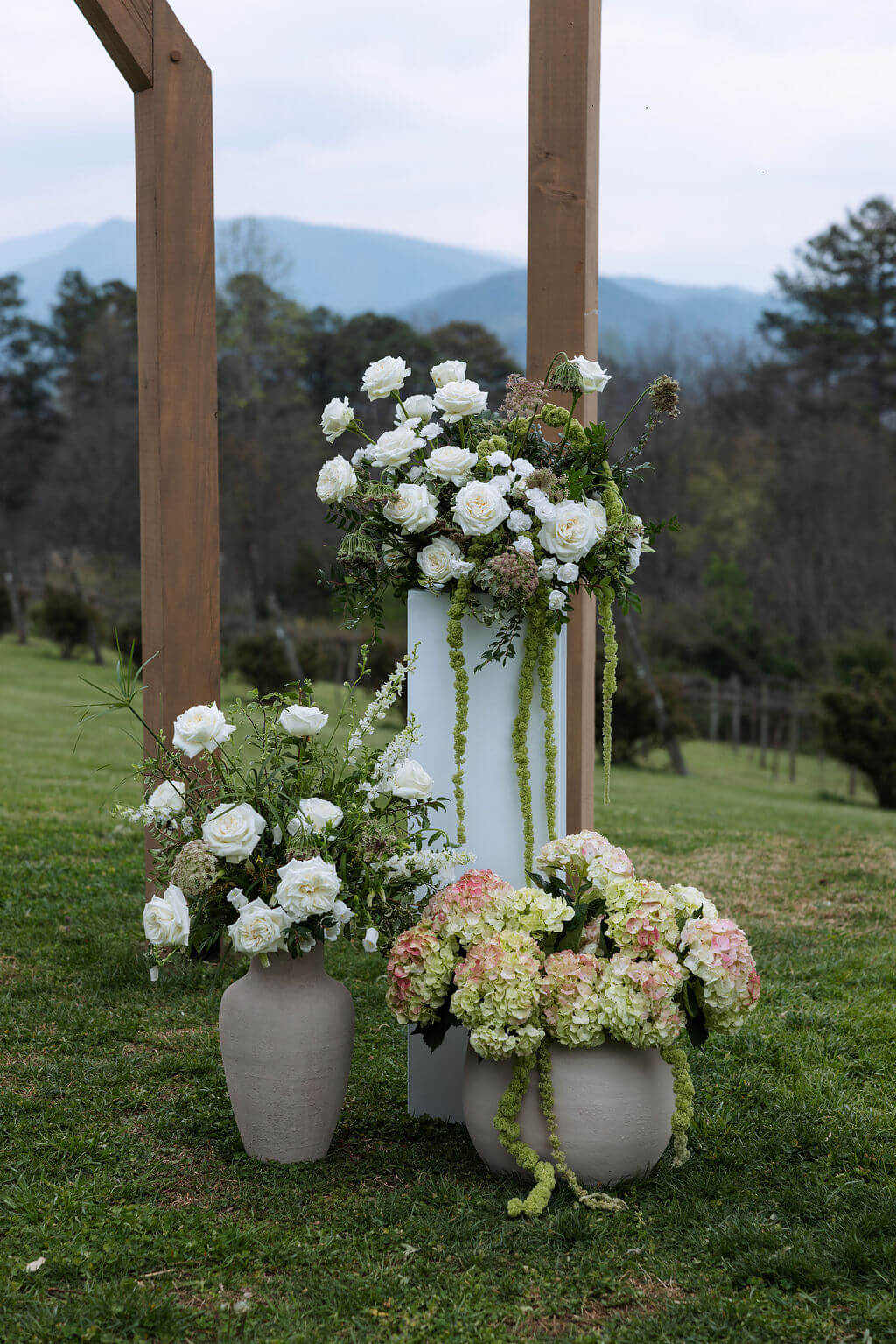 White and green floral arrangements decorate a wooden wedding ceremony structure with mountains in the distance.