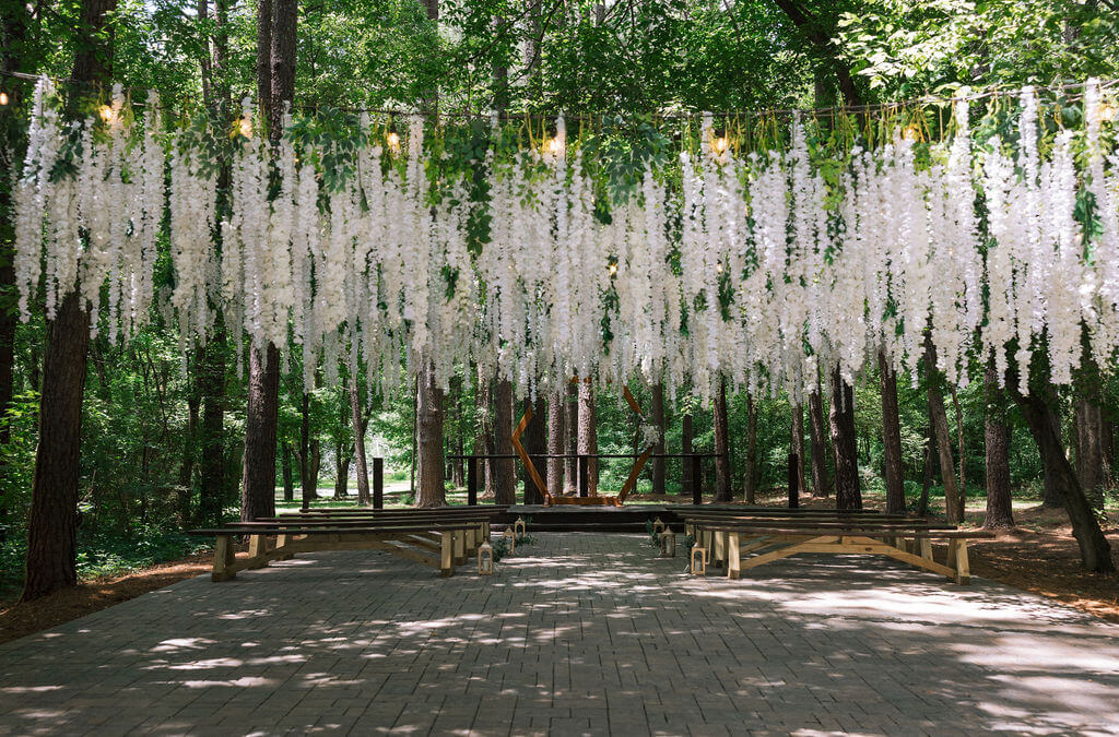 Woodland wedding ceremony space with wooden benches and cascading white flowers suspended between the trees.