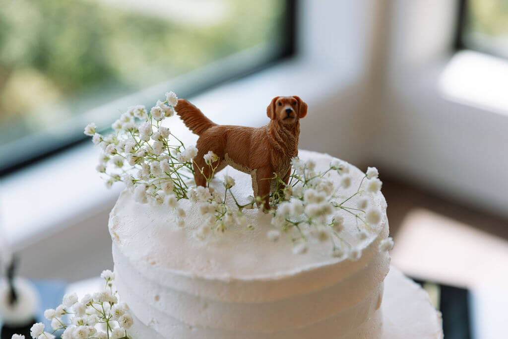 White wedding cake decorated with baby’s breath and a small golden retriever figurine as the cake topper.