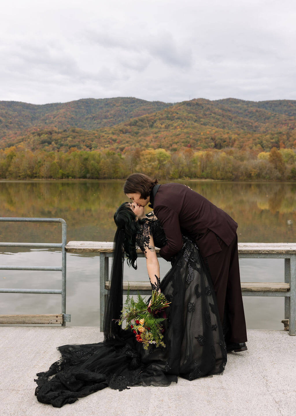 The couple kisses beside Cove Lake with fall-covered Tennessee mountains behind them on their wedding day.