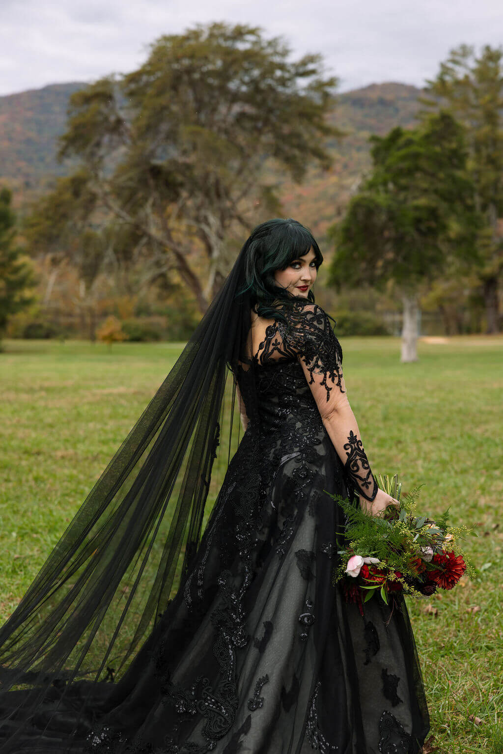 The bride poses in a dramatic black wedding gown and long black veil against the autumn landscape at Cove Lake State Park.