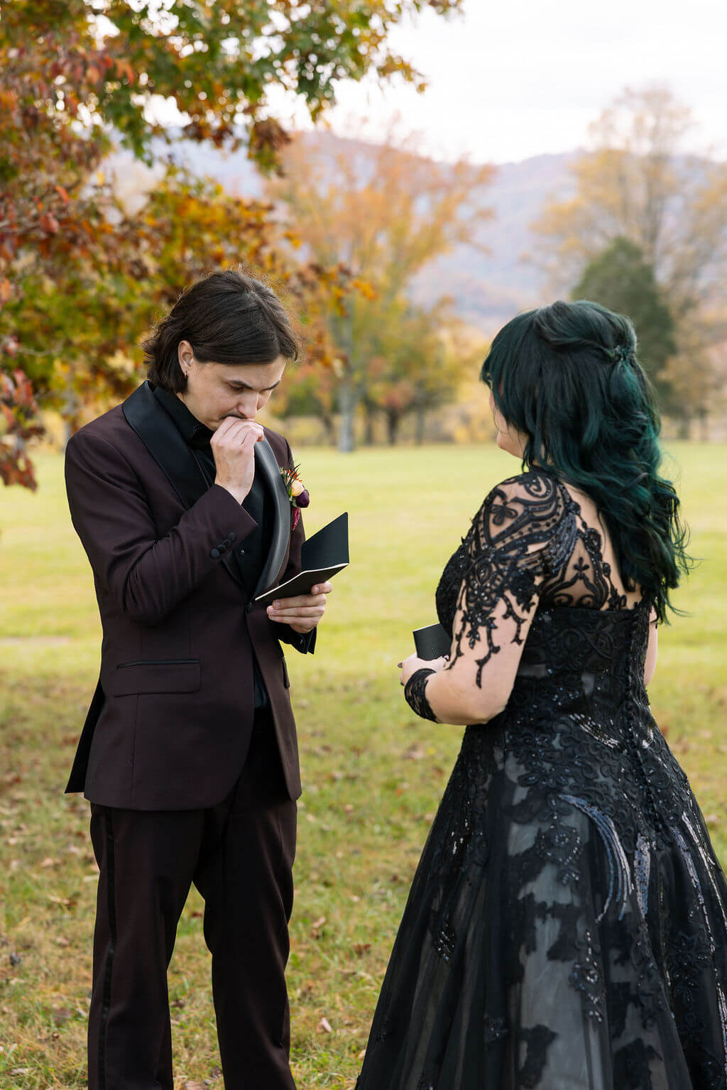The groom reads a handwritten note while the bride stands beside him in her black lace wedding gown.