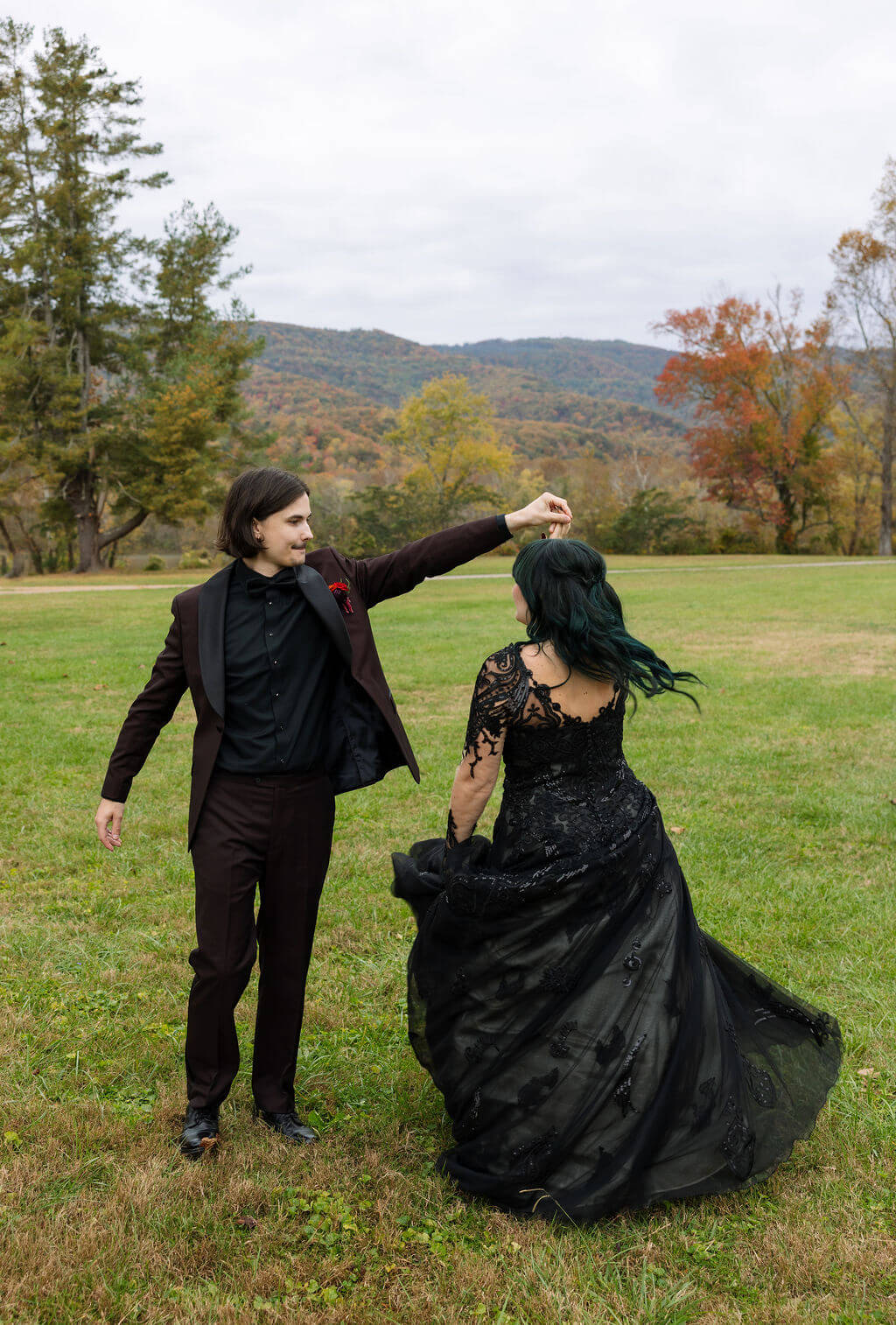 The couple dances together in a grassy field with colorful Tennessee mountains in the distance.