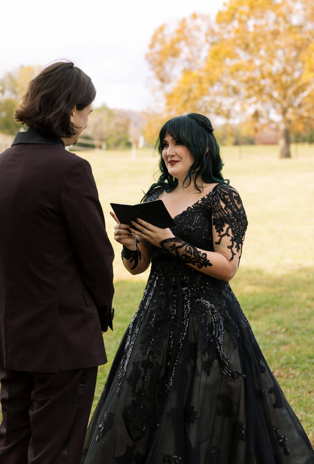 The bride reads from a card while the groom listens during a private moment before their outdoor wedding ceremony.