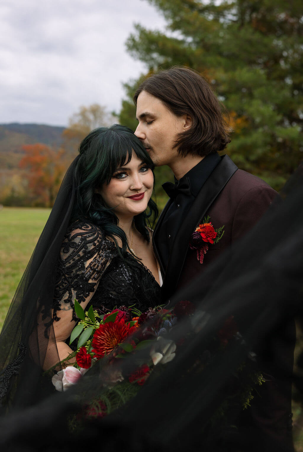 The groom kisses the bride’s forehead during a close wedding portrait with her black veil softly framing them.