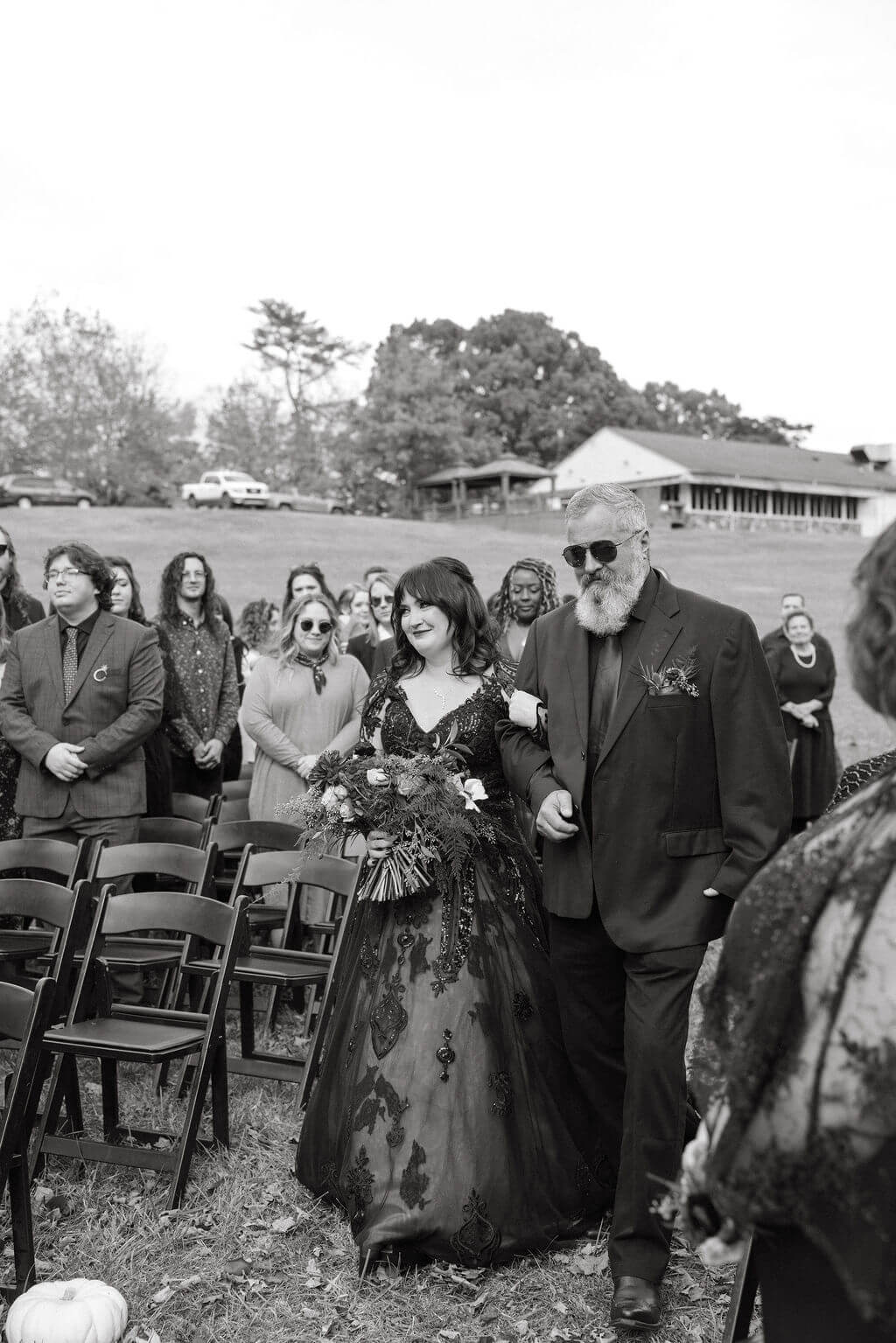 Black-and-white photo of the bride walking down the aisle in her black wedding dress as guests watch.