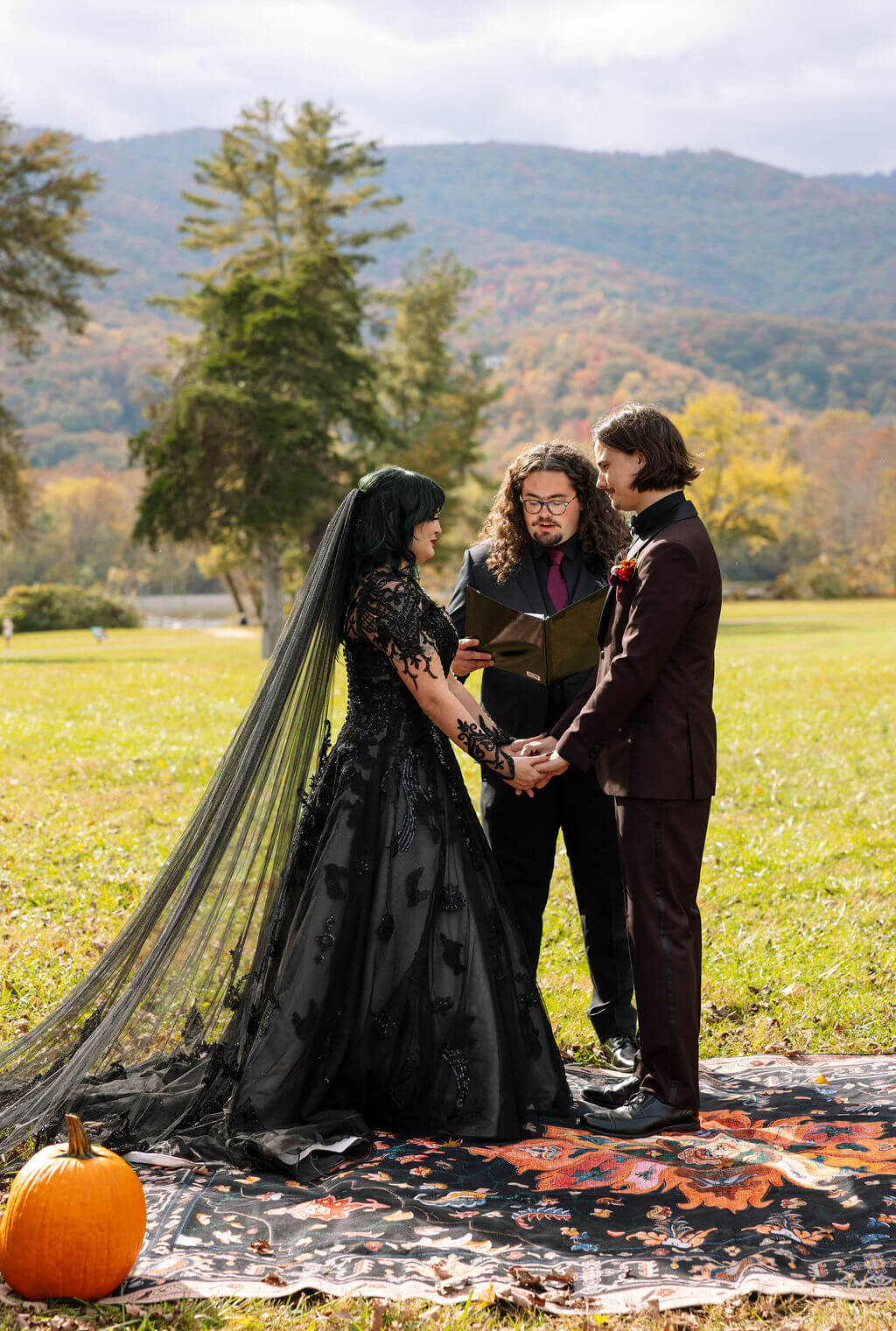 The couple holds hands during their outdoor ceremony with colorful Tennessee mountains behind them.