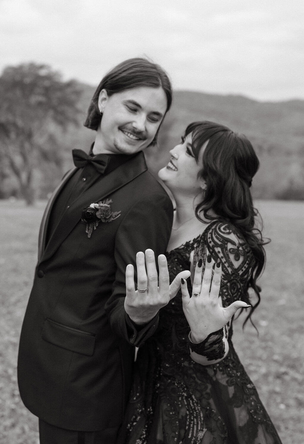 Black-and-white portrait of the couple smiling together while showing off their wedding rings.