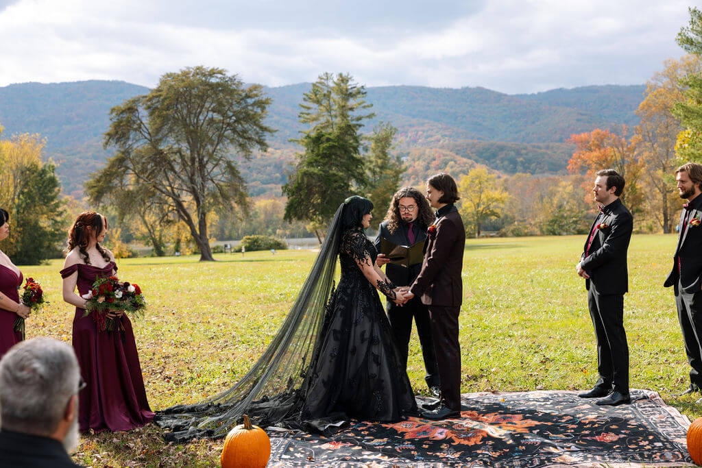 Wide view of an outdoor fall wedding ceremony with guests, pumpkins, trees, and mountain views.