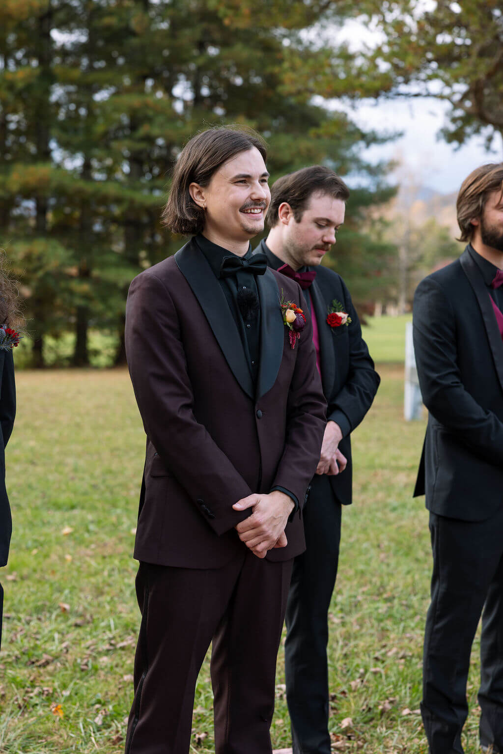 The groom smiles while waiting with a member of his wedding party before the outdoor ceremony begins.