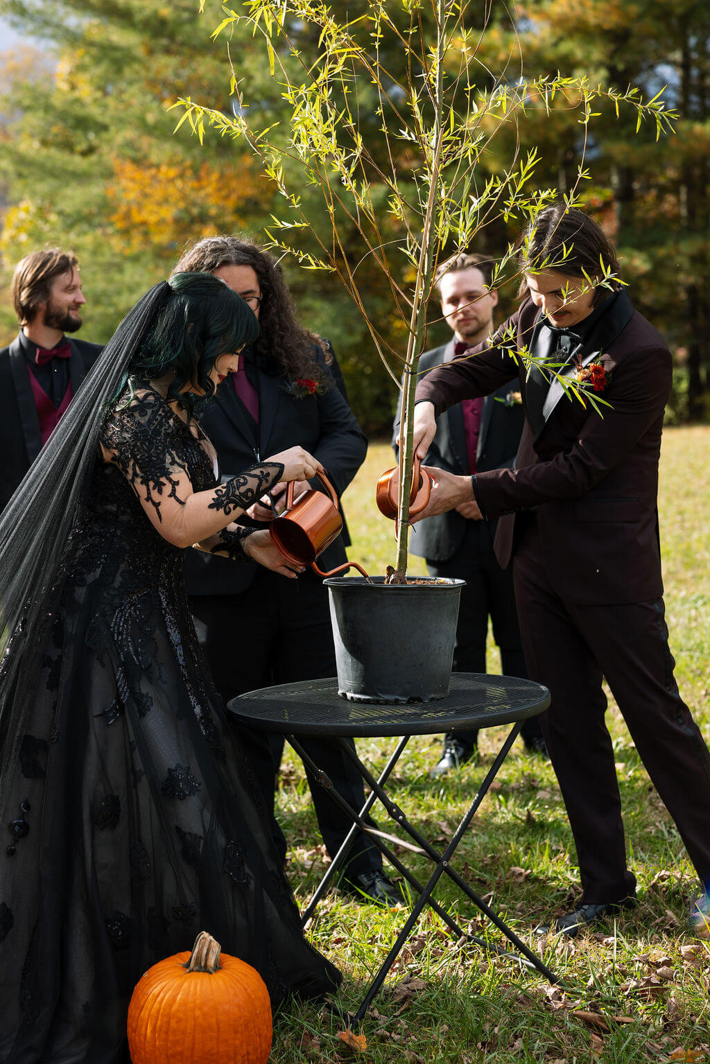 The bride and groom use rose gold watering cans to water a tree during emotional fall wedding ceremony