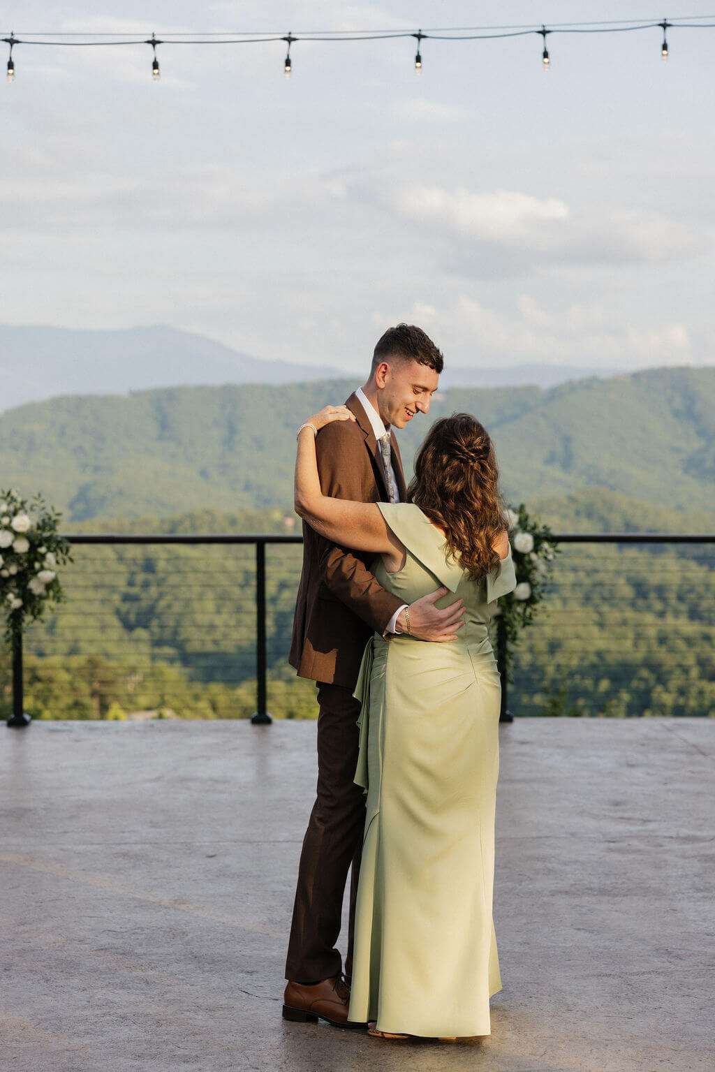 Groom dancing with a woman in a light green dress during the outdoor wedding reception.