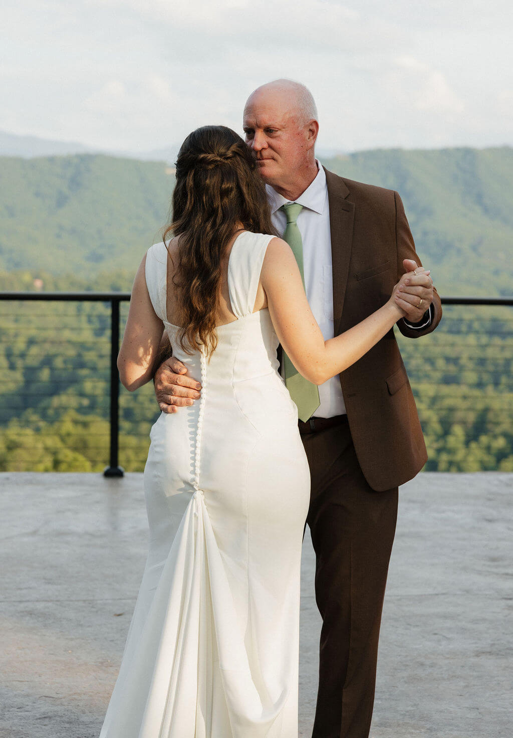 Bride dancing with an older man outdoors with the Smoky Mountains in the background.