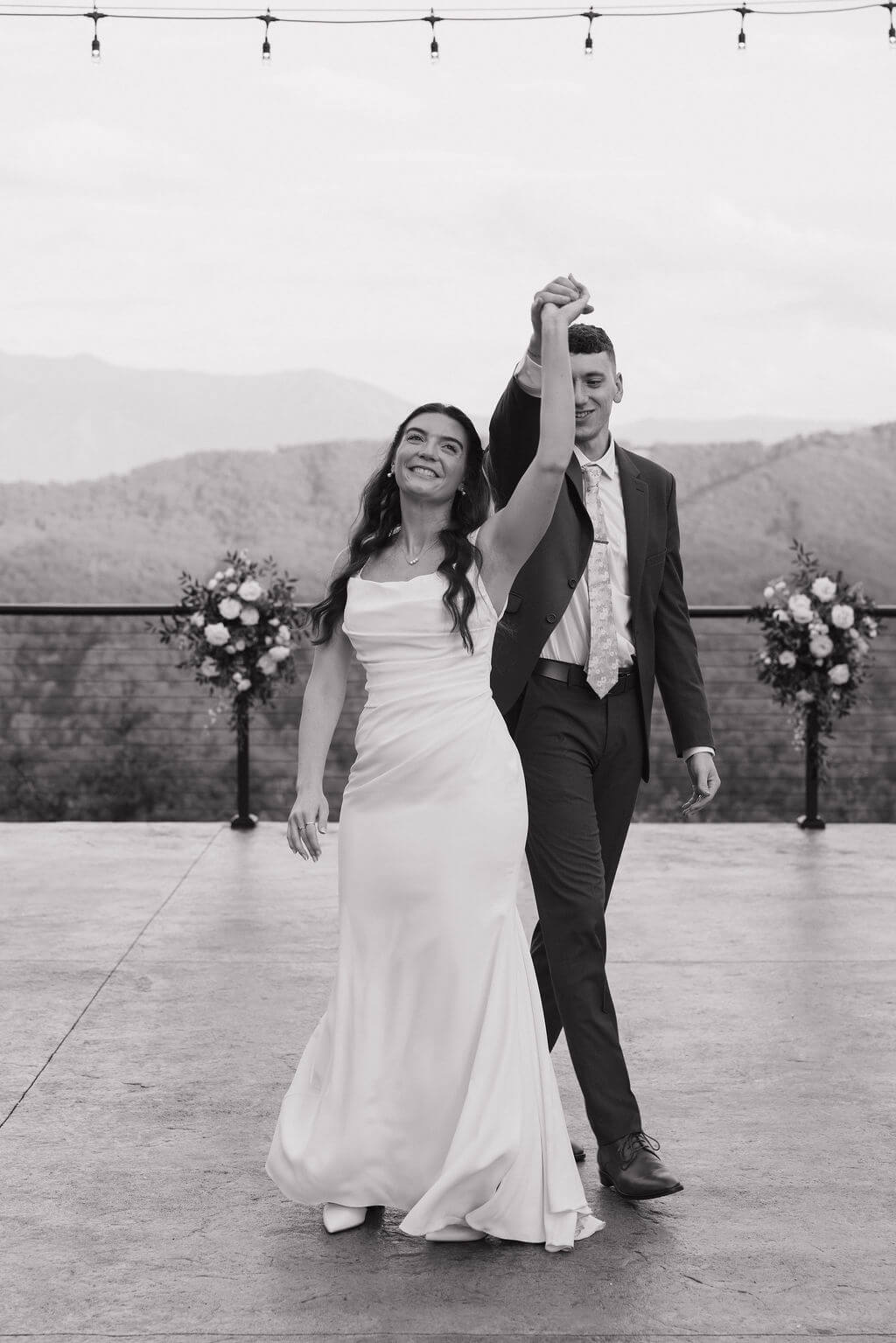 Black-and-white photo of the groom twirling the smiling bride on the outdoor ceremony terrace.
