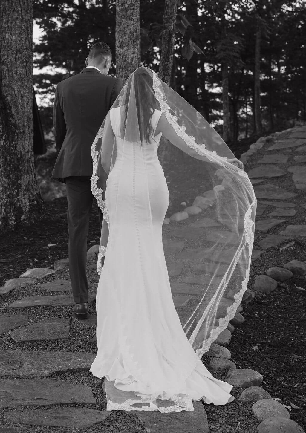 Black and white image of a bride and groom walking on a winding stone path