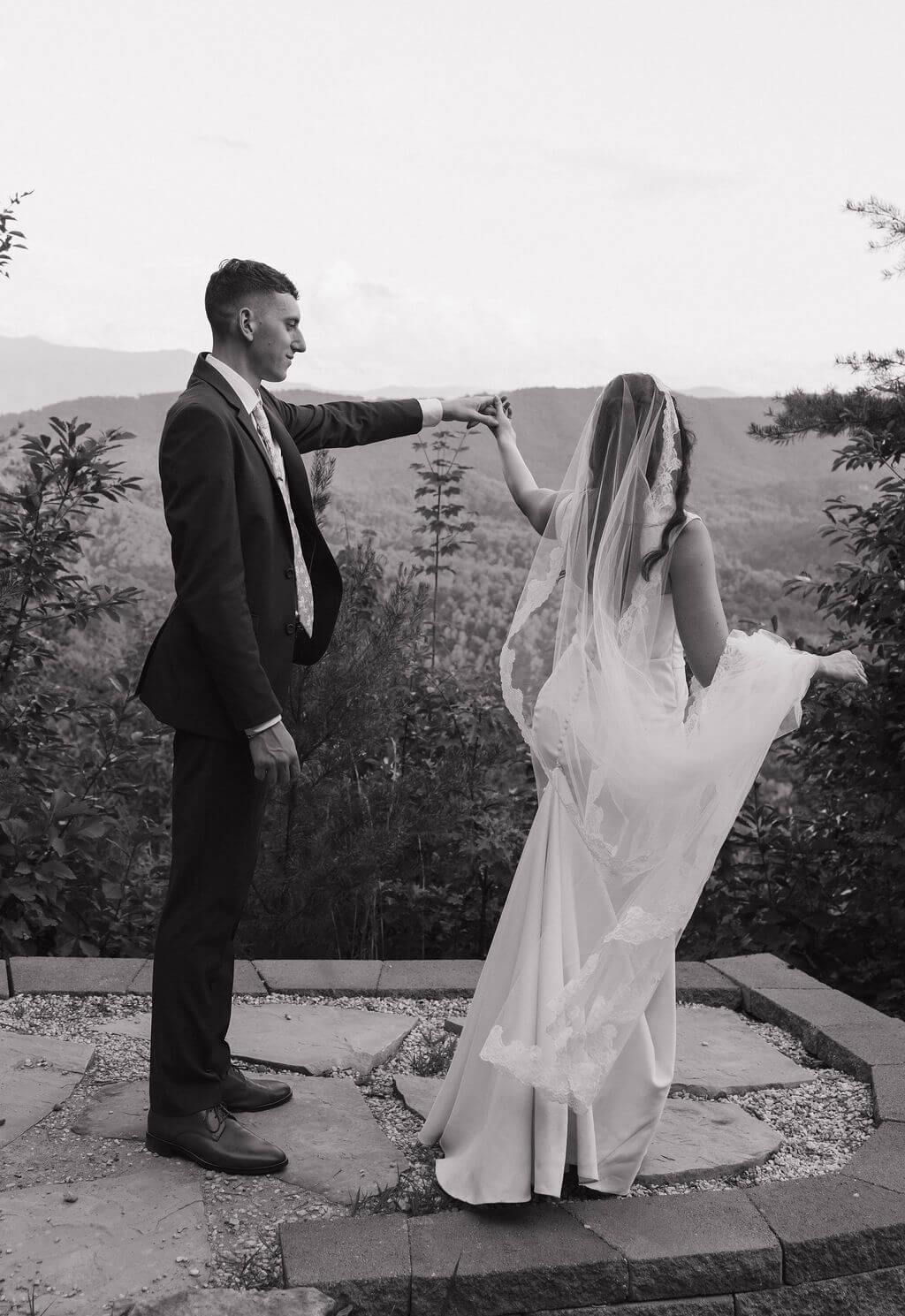 Black-and-white photo of the groom twirling the bride during portraits at a mountain overlook.