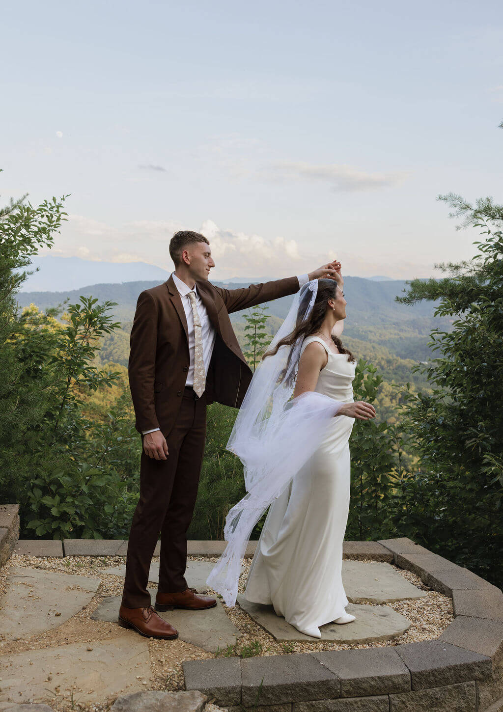 Groom twirling the bride by her veil during wedding portraits overlooking the Smoky Mountains.