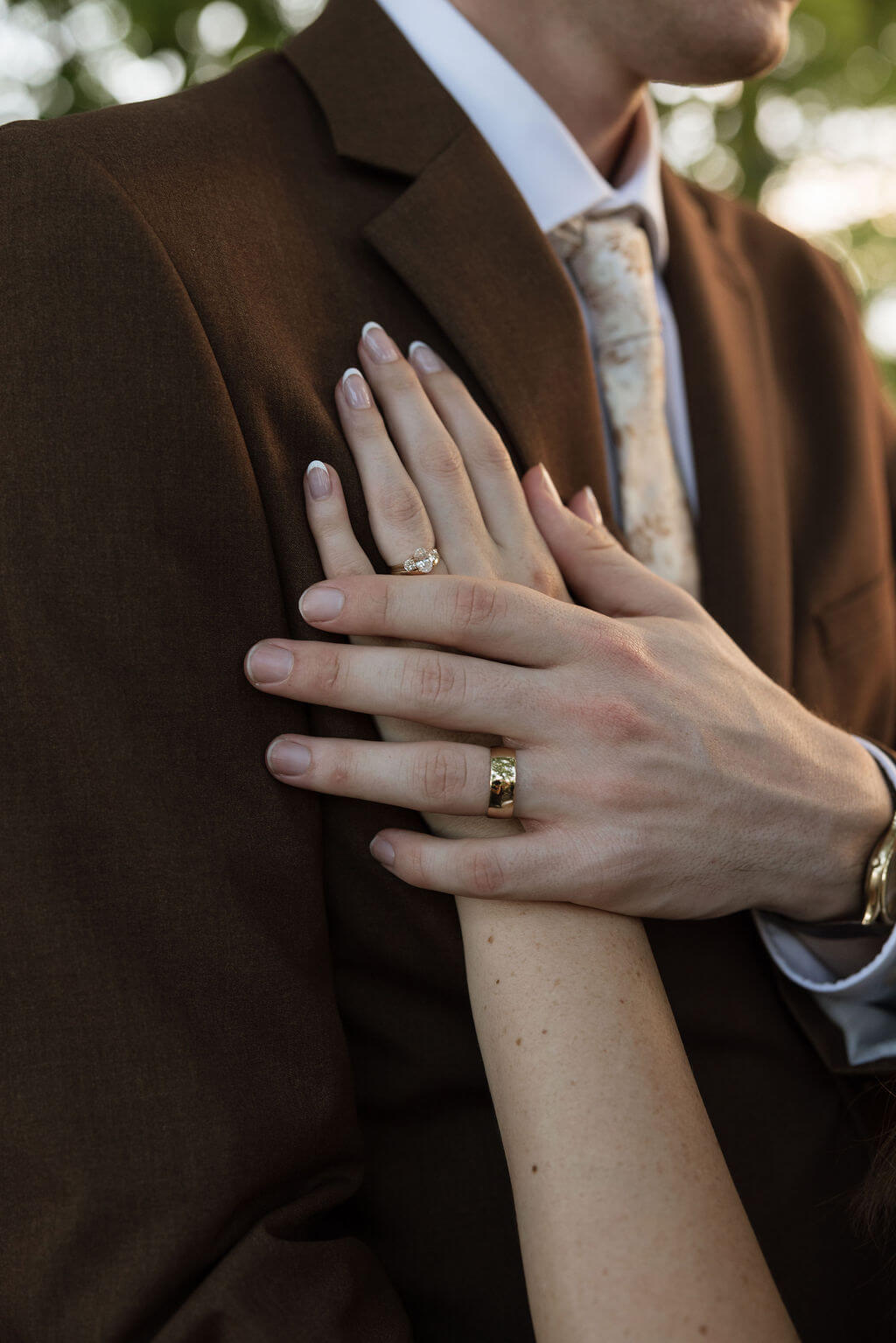 Close-up of the bride’s hands resting on the groom’s brown suit, showing their wedding rings.