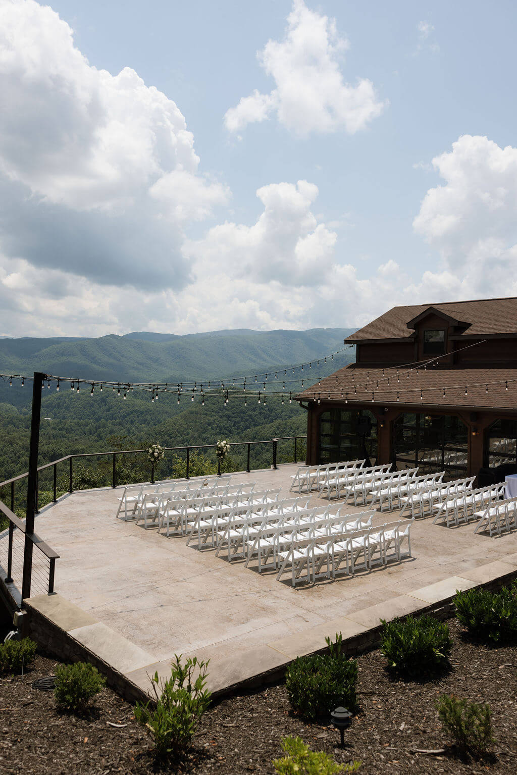 Outdoor wedding ceremony setup with rows of white chairs, string lights, and panoramic Smoky Mountain views.
