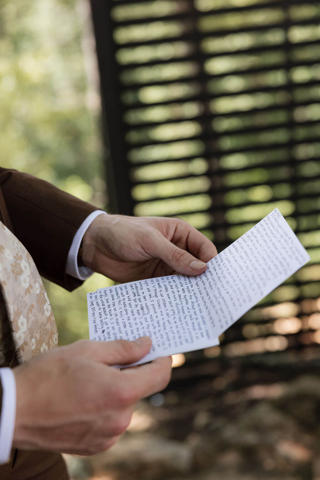Close-up of the groom holding and reading a handwritten wedding letter outdoors.