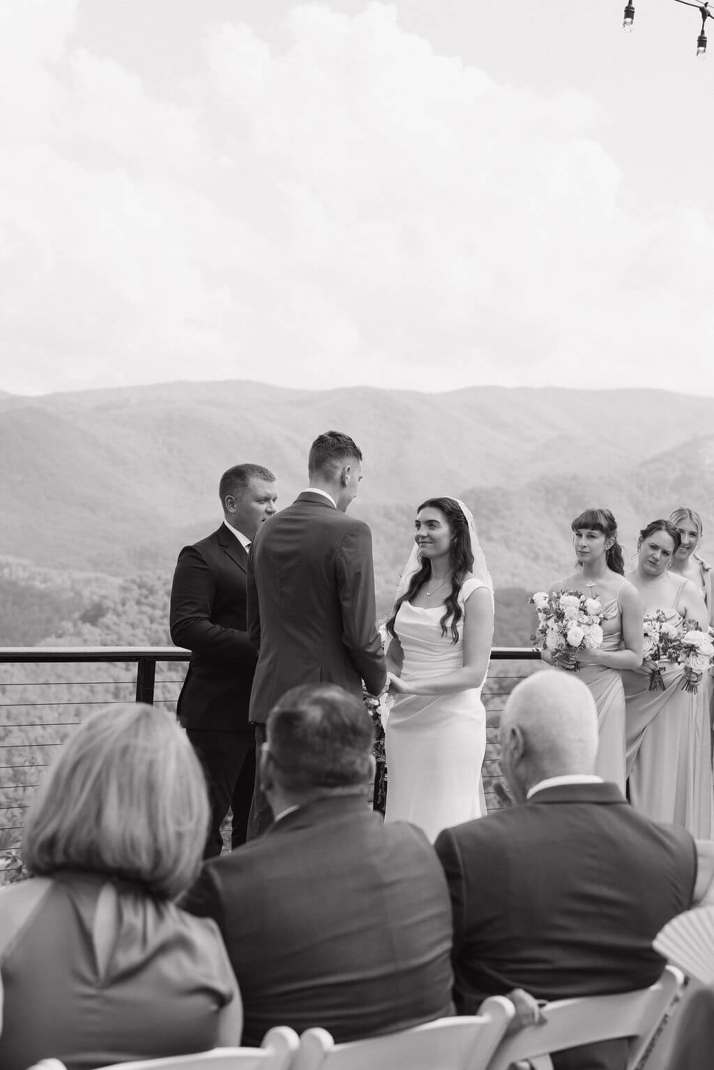 Black-and-white view of the bride and groom facing each other during their ceremony with guests seated in the foreground.