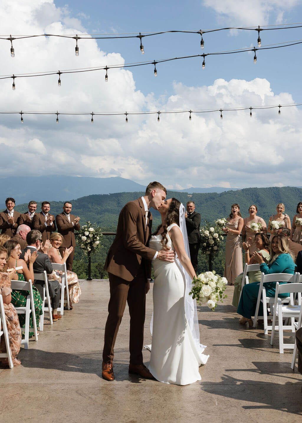 Bride and groom share a kiss while walking down the aisle surrounded by their guests