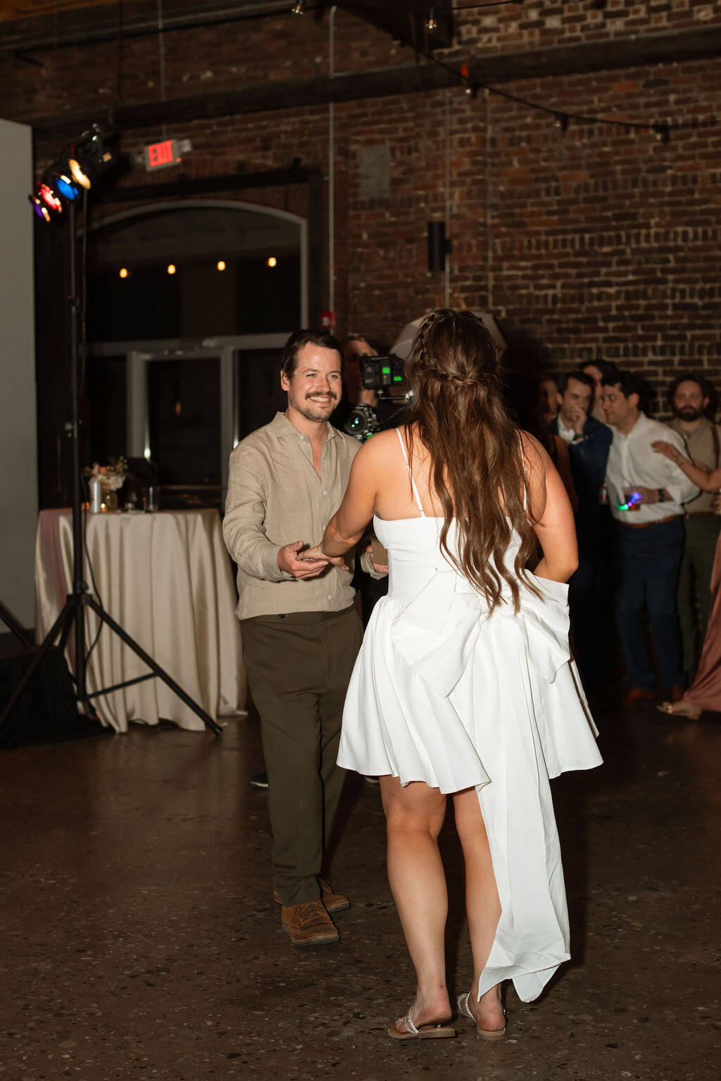 Bride in her bustled gown heading onto the dance floor toward a guest during the reception
