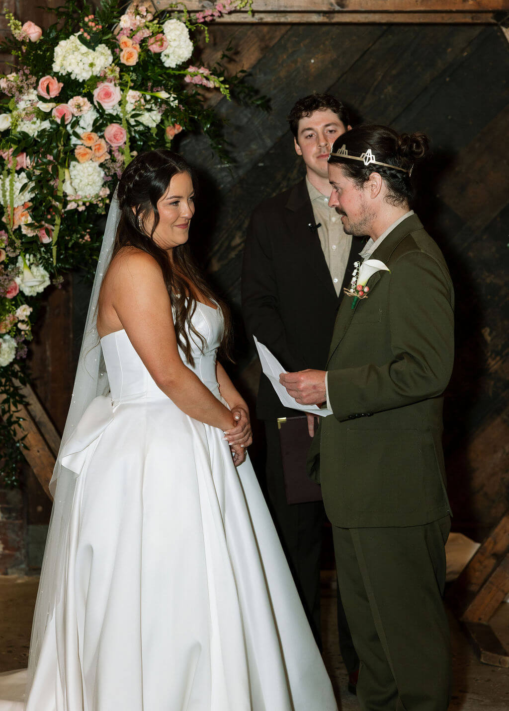Groom reading his vows to the bride in front of the floral hexagon arch while the officiant looks on