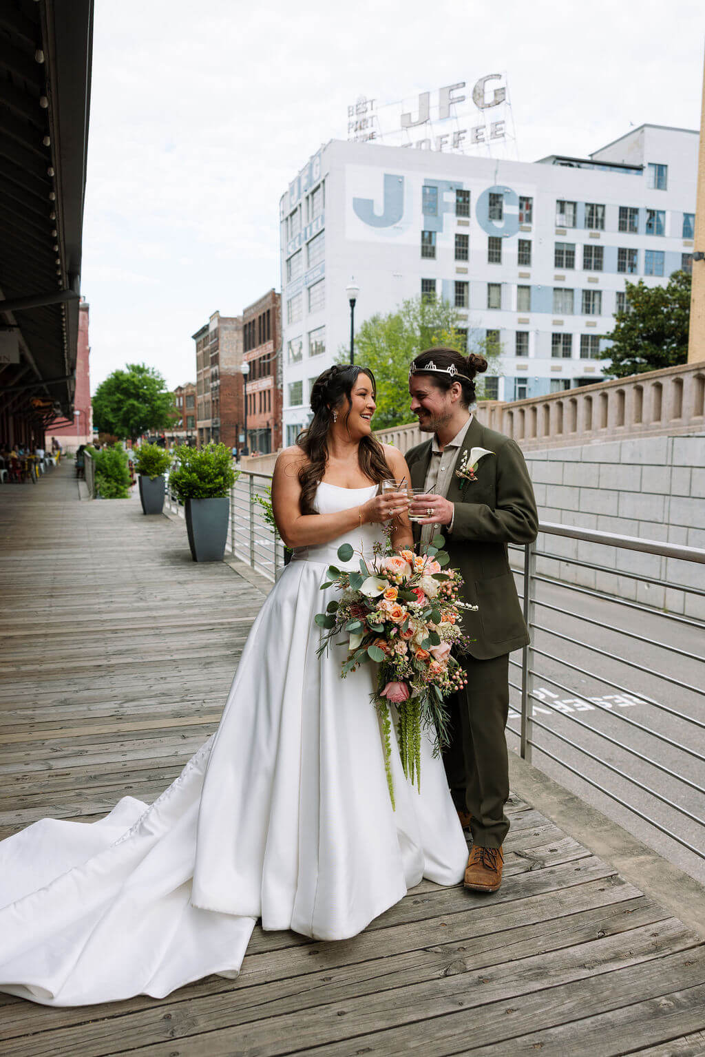 Bride and groom smiling and toasting with champagne on the wooden platform with the JFG Coffee building in the background