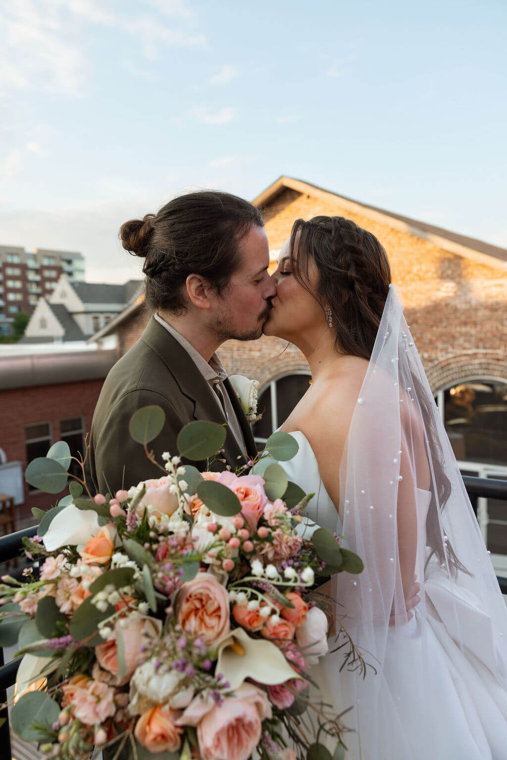 Bride and groom kissing with the brick roofline of Jackson Terminal behind them and the bride's bouquet in the foreground