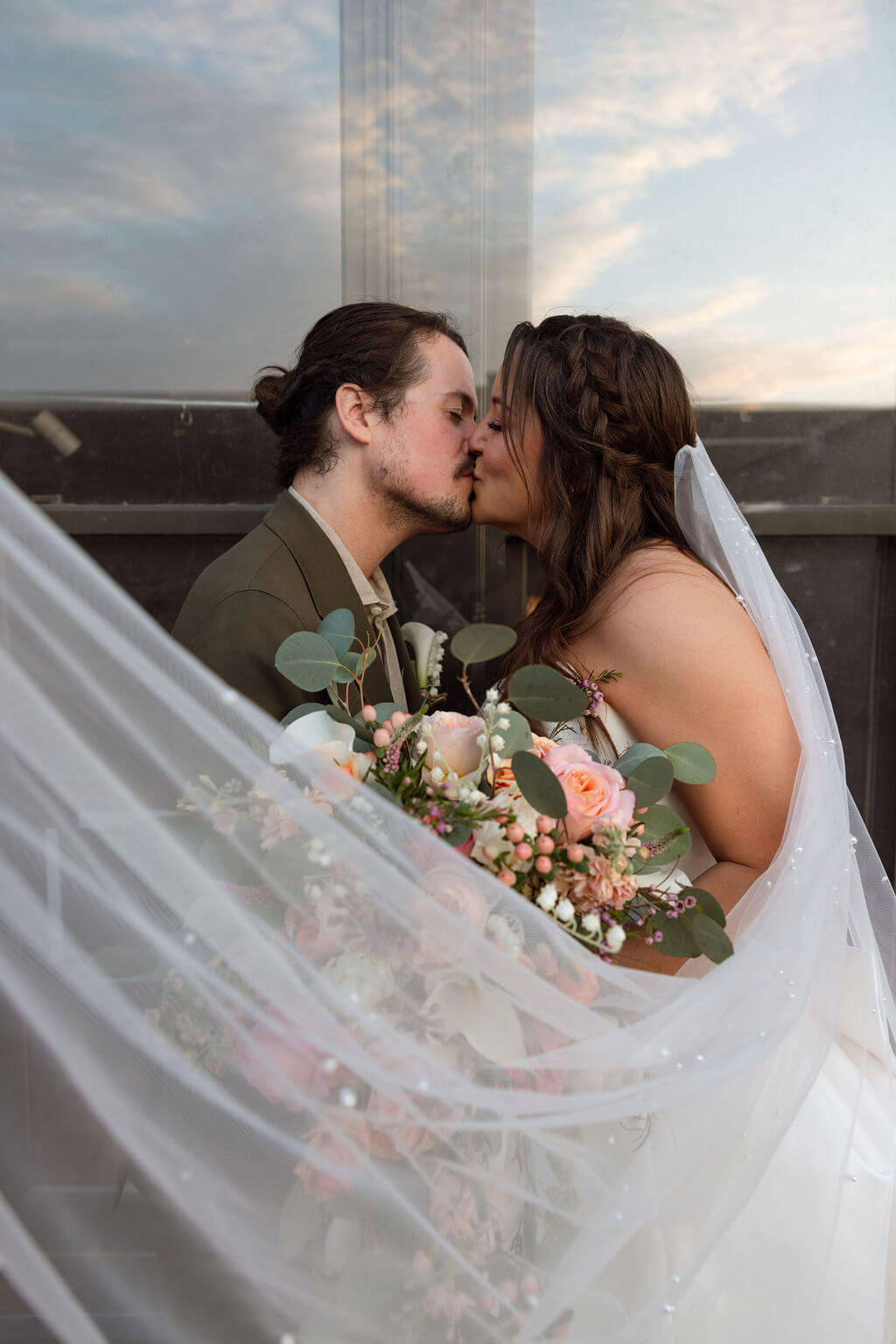 Bride and groom kissing as the bride's veil sweeps across the frame with her bouquet between them