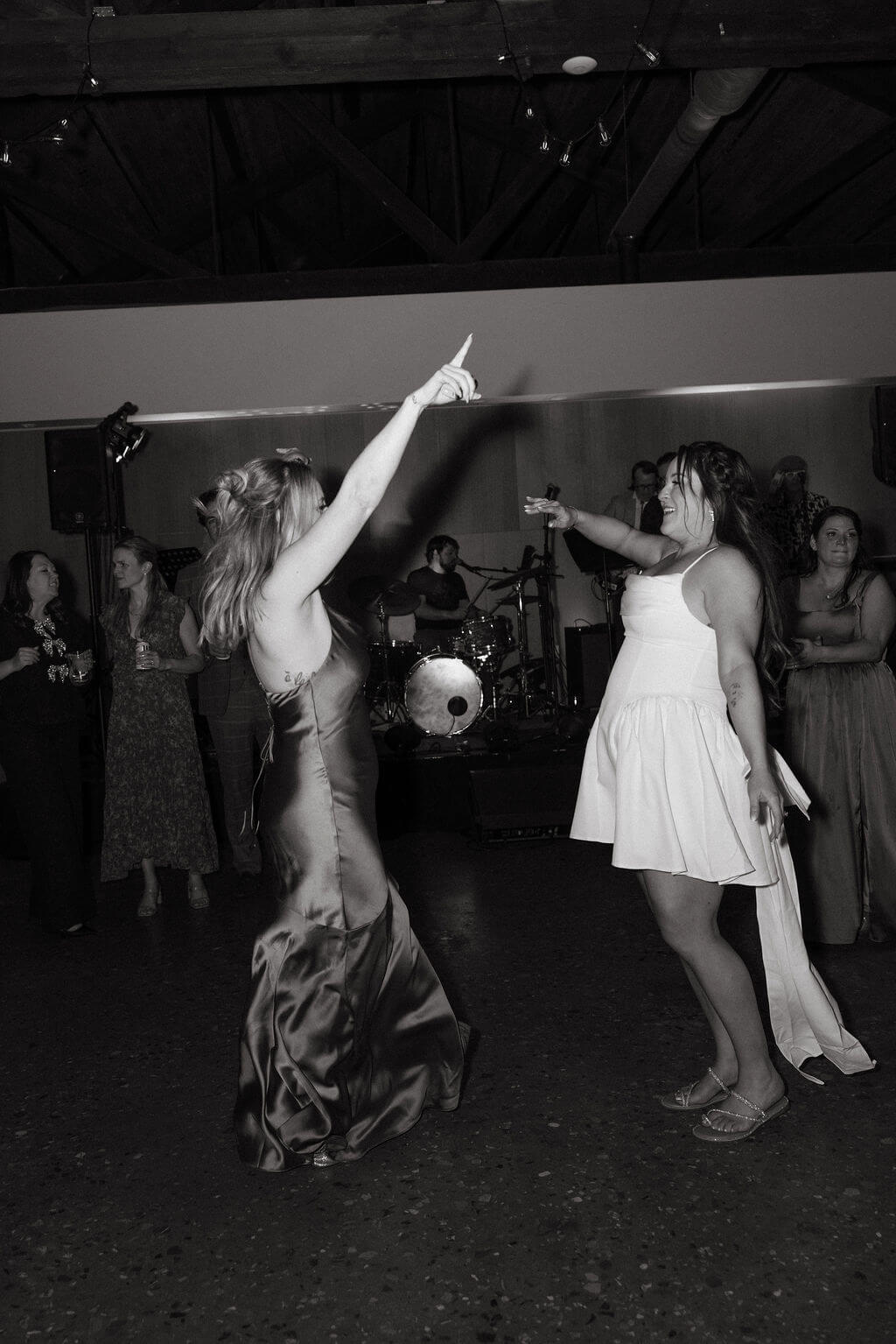 Black and white photo of the bride and a guest dancing with their arms raised on a crowded dance floor