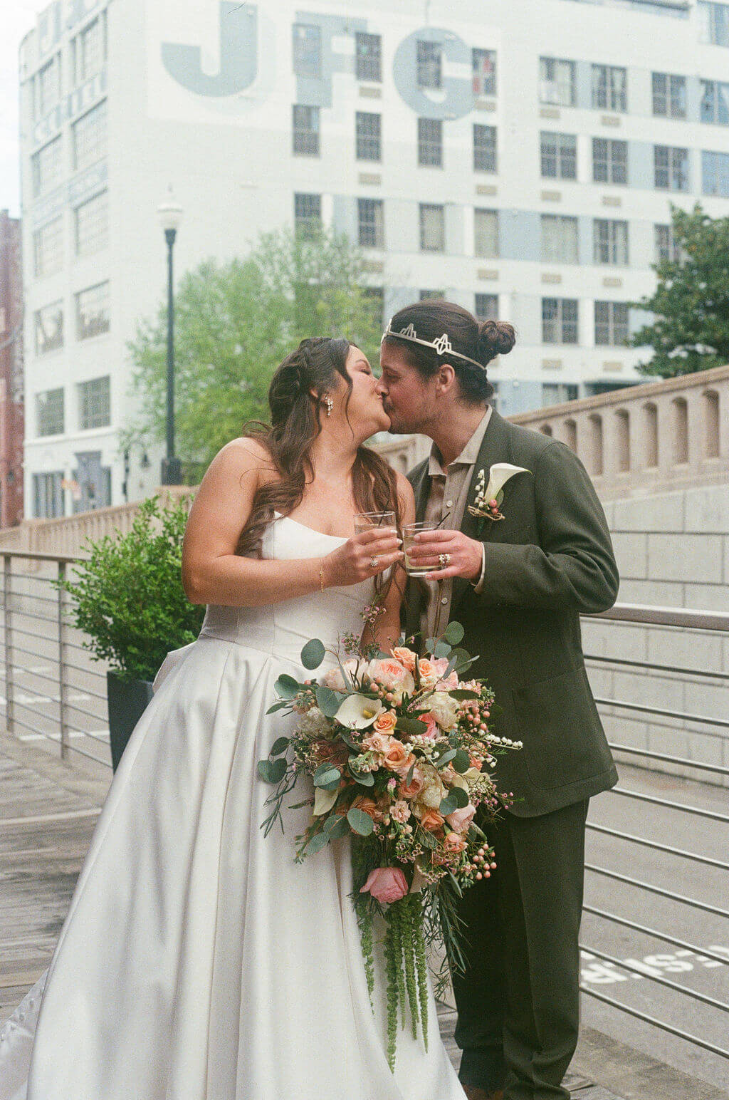 Bride and groom kissing while holding champagne glasses on the Jackson Terminal platform with the historic JFG Coffee building behind them