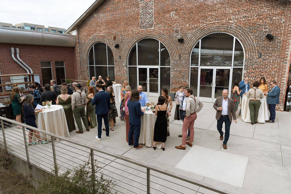 Wedding guests mingling around high top cocktail tables on the patio outside Jackson Terminal's arched brick windows