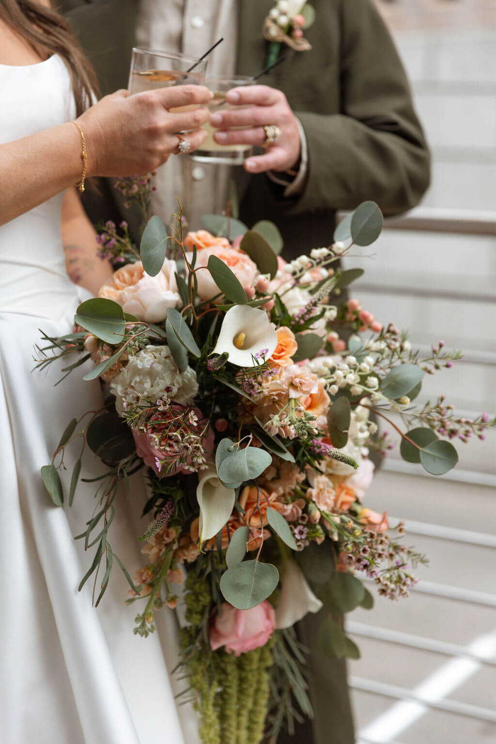 Close-up of the bride and groom clinking cocktail glasses with the bride's colorful bouquet in the foreground