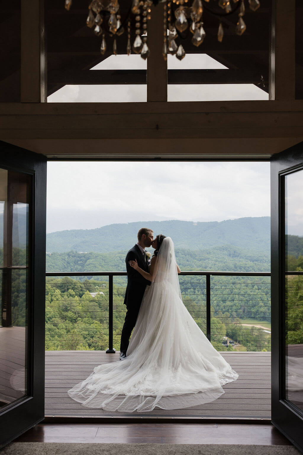 Bride and groom kissing on a covered balcony at The Magnolia with the Smoky Mountains in the distance.
